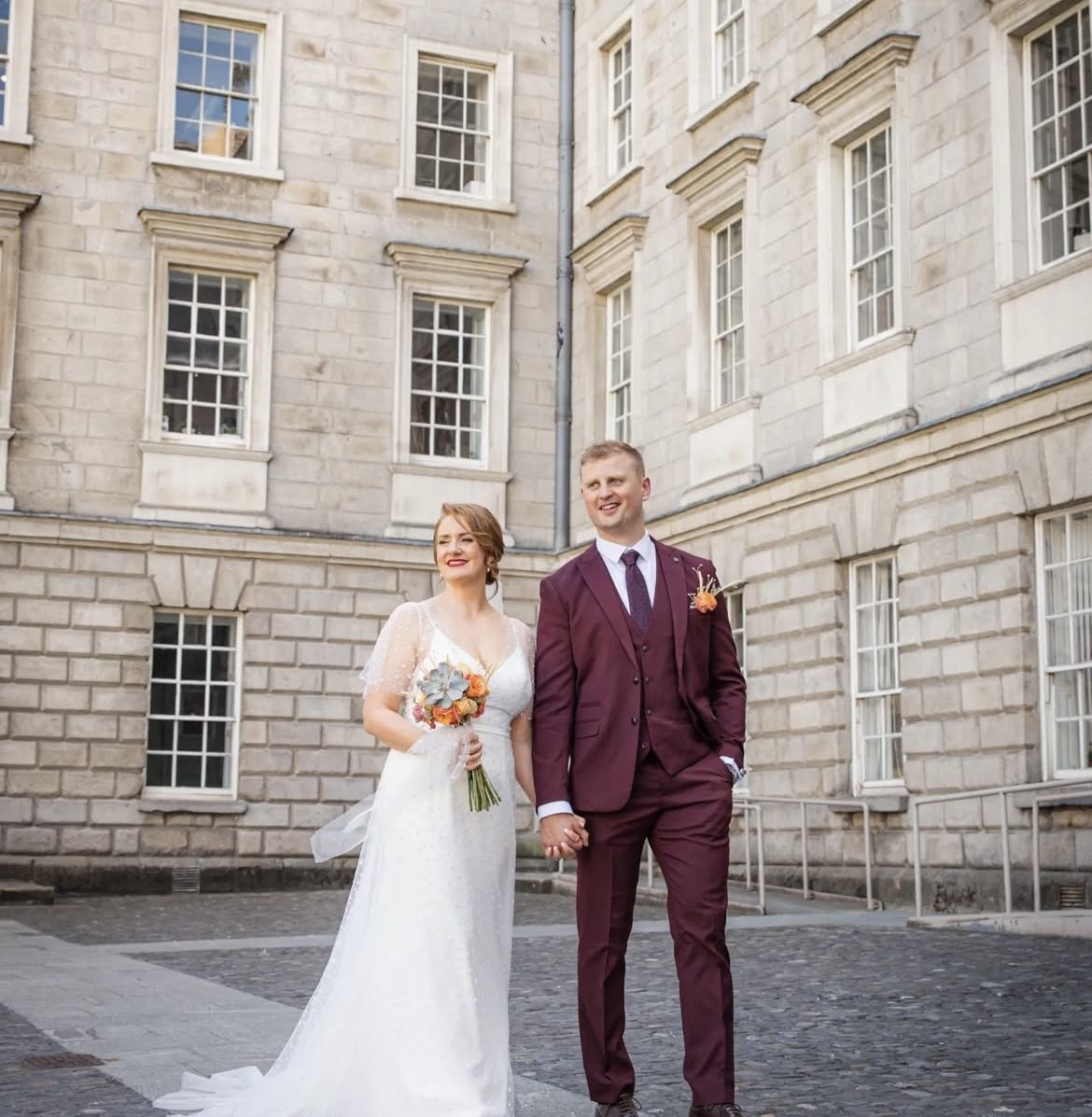 Groom in a burgundy three-piece suit with his bride in a Dublin courtyard
