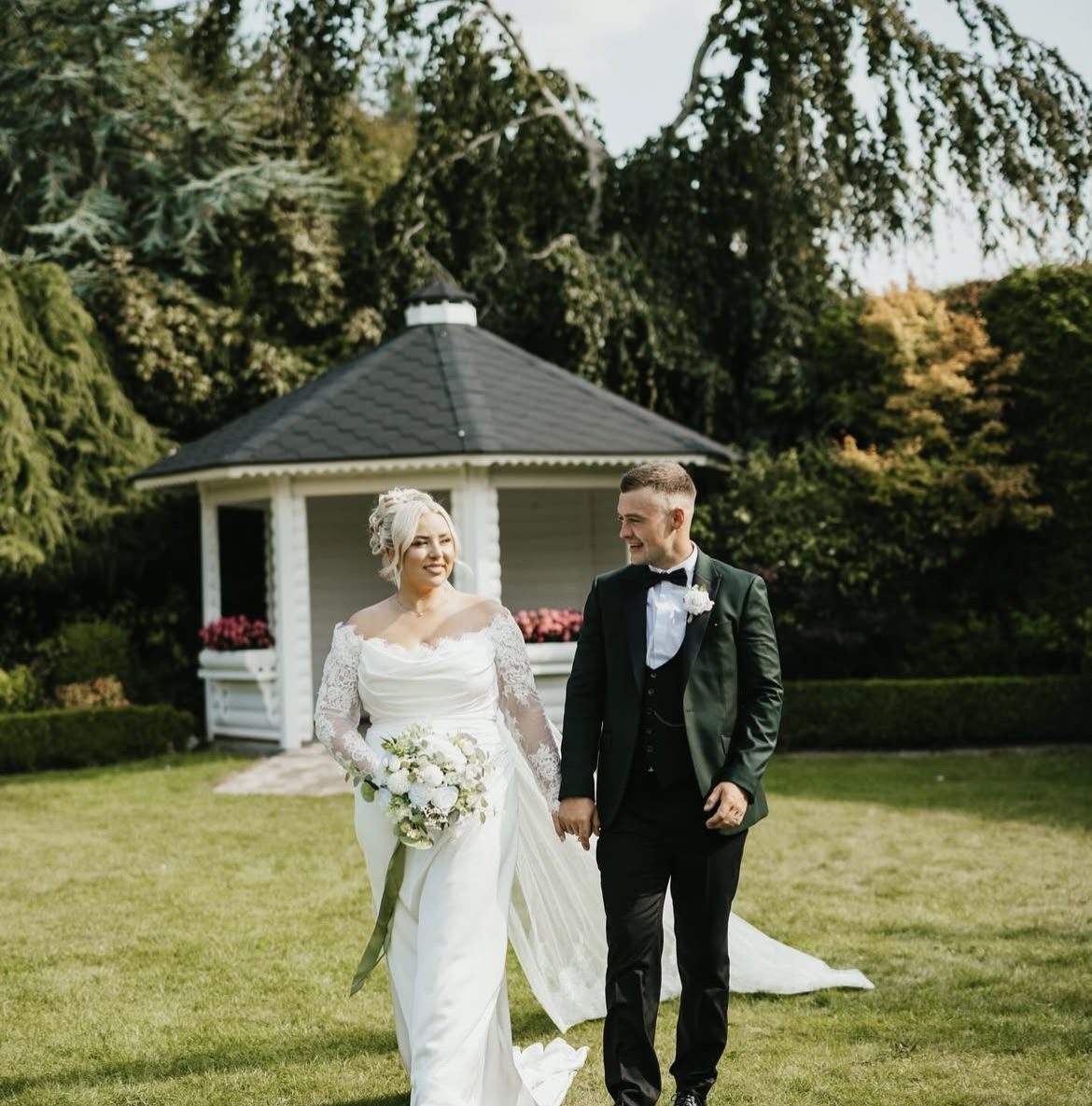 Groom in a dark green tuxedo with his bride on a lawn