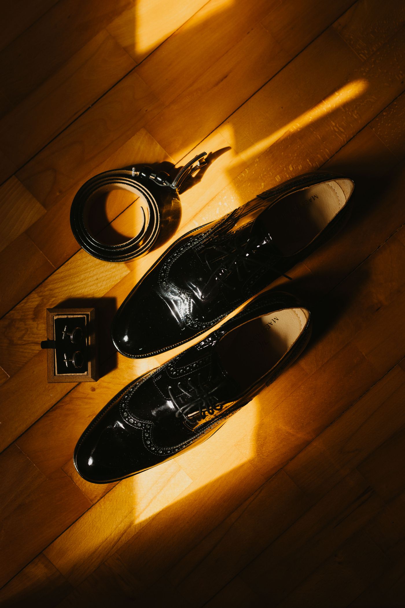 Black formal shoes, belt and cufflinks arranged on a wooden floor