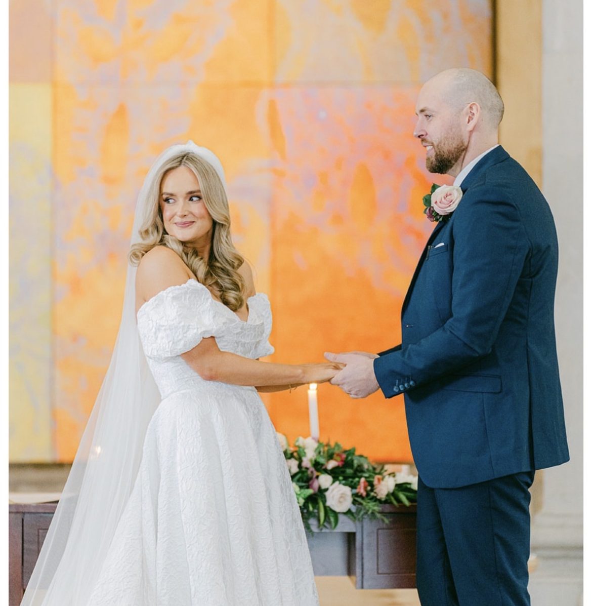 Groom in a navy suit holding hands with his bride at the ceremony